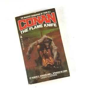 May include: A paperback book cover featuring a red and white illustration of Conan the Barbarian, a fictional character, with the title "Conan The Flame Knife" and the author's name "Robert E. Howard and L. Sprague de Camp".