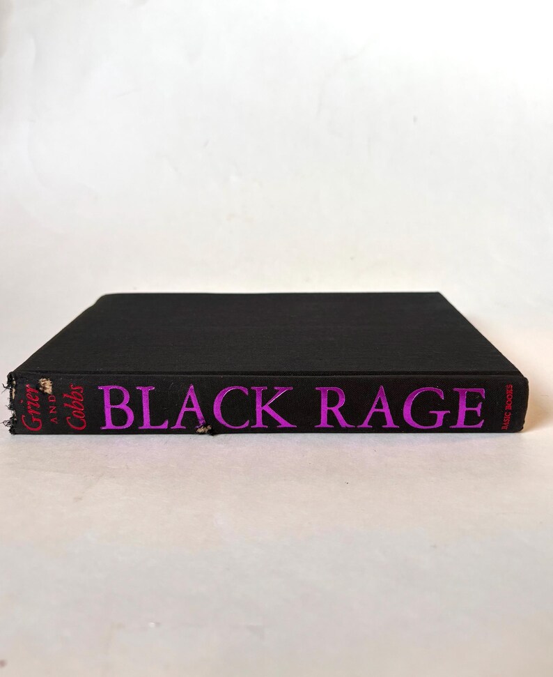 K&ouml;nnte beinhalten: Ein schwarzes Hardcover-Buch mit dem Titel "BLACK RAGE" in leuchtend rosa Buchstaben. Der Buchr&uuml;cken zeigt auch die Namen der Autoren, "Grier and Cobbs", in Rosa. Das Buch ist vor einem wei&szlig;en Hintergrund platziert.
