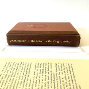 May include: A hardcover edition of "The Return of the King" by J.R.R. Tolkien. The book has a brown cover with gold lettering and a circular design. The title and author's name are visible.