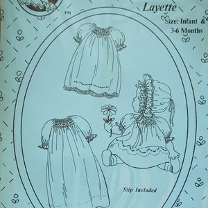 May include: A light blue pattern for a baby's smocked layette, featuring illustrations of baby dresses and a baby holding a flower. The text reads "The Old Fashioned Baby" and "Baby's Smocked Layette". Size: Infant & 3-6 Months.
