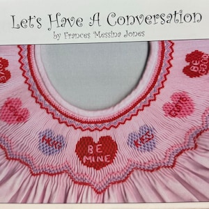 May include: A pink garment with a ruffled collar, featuring embroidered hearts with phrases like "BE MINE" and "KISS". The text "Let's Have A Conversation" and the designer's name are at the top. The design is a mix of pinks and reds.