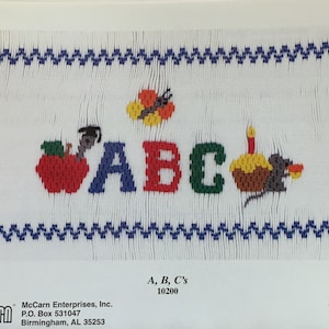 May include: Cross-stitch sampler with the letters "ABC" in red, blue, and green, with a red apple, a butterfly, and a cupcake with a candle. The design is framed by blue zig-zag borders. Text at the bottom reads "A, B, C's".