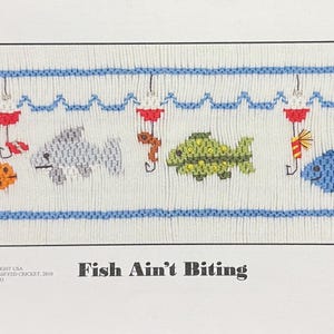 May include: A rectangular cross-stitch design featuring five colorful fish and fishing bobbers. The fish are orange, gray, green, and blue, with blue and white wavy lines above and below. The text "Fish Ain't Biting" is below the design.