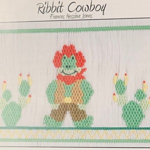 May include: A cross-stitch design featuring a frog cowboy character with a red bandana and hat, green vest, and brown pants. Two green cacti flank the frog. The text "Ribbit Cowboy" and the artist's name are at the top.