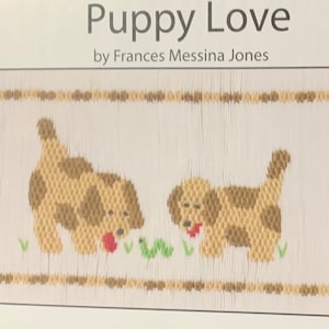 May include: A framed artwork titled "Puppy Love" by Frances Messina Jones. The image features two tan and brown puppies with red tongues, embroidered on a white background. Green grass and a worm are also depicted.