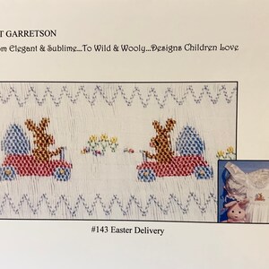 May include: A white fabric design featuring two embroidered bunnies in red vehicles, each carrying a blue and white egg. The text "#143 Easter Delivery" is at the bottom. The image also includes a small inset of a white dress.
