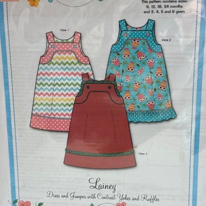 May include: A sewing pattern for a dress and jumper with contrast yokes and ruffles. The pattern includes sizes for children aged 6 months to 6 years. The design features three different dress styles with various patterns and colors, including chevron, owls, and solid red.