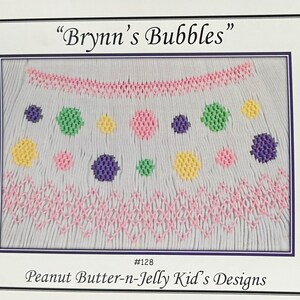 May include: Embroidered design titled "Brynns Bubbles" featuring a pattern of pink, yellow, green, and purple circles and zigzags. The design is on a white background and is framed in a white mat.