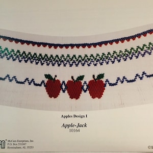 May include: A white fabric design featuring rows of embroidered patterns in blue, green, and red. Three red apples with green leaves are centered at the bottom. The text "Apples Design I" and "Apple-Jack" are visible.