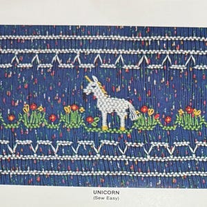 May include: A blue fabric panel with a white unicorn design. The unicorn is surrounded by embroidered flowers and greenery. The text "UNICORN (Sew Easy)" is visible at the bottom of the image.