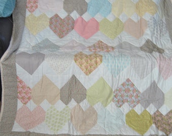 May include: A white quilt with a patchwork design featuring a variety of pastel colors and floral patterns. The quilt is made up of heart-shaped pieces arranged in a geometric pattern.