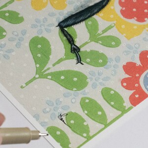 May include: A close-up of a colorful floral print with green leaves and white dots. The print features a black and white illustration of a bird with a long, thin leg.
