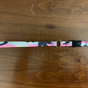 May include: A pink, black, and white camouflage patterned key chain with a black plastic clip and a silver metal ring.