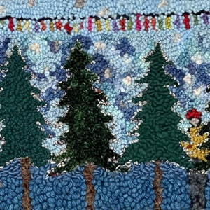 May include: A rug hooking artwork depicting a winter scene with five green pine trees, a blue sky with white clouds, and a small figure in a red hat and yellow clothing standing in front of the trees. The trees are rooted in a blue and white snow-covered ground.