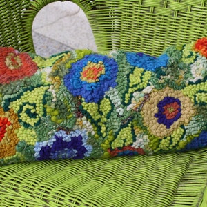 May include: A colorful floral patterned pillow with a green, blue, yellow, orange, and red color scheme. The pillow is sitting on a green wicker chair.