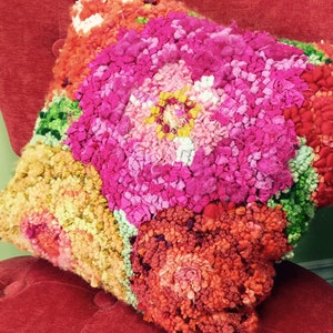 May include: A colorful, handmade pillow with a floral design. The pillow is made of a variety of textures and colors, including pink, orange, yellow, and green.
