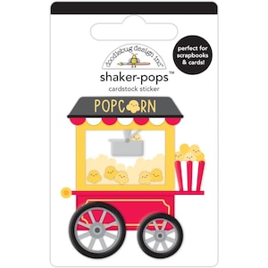 May include: A cardstock sticker featuring a popcorn cart design. The cart is red and yellow with a black roof and the word "POPCORN" on top. The sticker is labeled "shaker-pops" and is perfect for scrapbooks and cards.