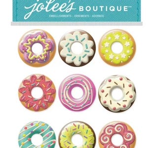 Puede incluir: Nueve adornos con forma de donut en varios colores, incluyendo rosa, amarillo y marrón. Cada donut tiene un diseño diferente de glaseado y chispas. El paquete incluye el texto "Jolee's Boutique" y "9 PC / PZ".