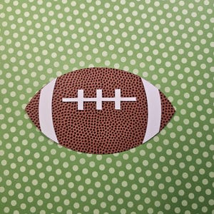 Puede incluir: Una pelota de fútbol marrón y blanca con cordones sobre un fondo de lunares verdes.