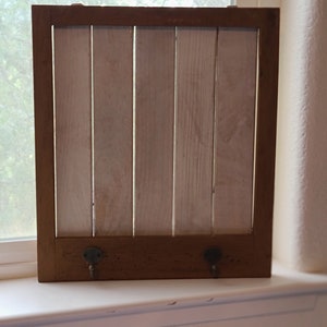 May include: A rustic wooden wall-mounted rack with two hooks. The rack is painted white and has a brown wood frame.