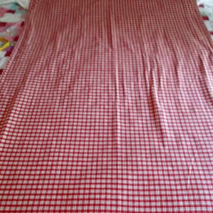 May include: Red and white gingham fabric with a fine checkered pattern. The fabric is smooth and appears to be woven.