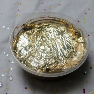 May include: A clear plastic container filled with a brown substance covered in gold foil.