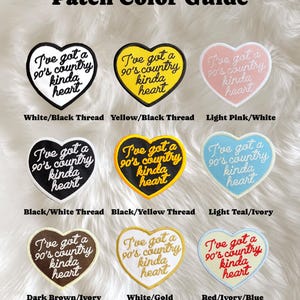 May include: A colour guide for iron-on patches featuring a heart-shaped design with the text "I've got a 90's country kinda heart". The patches are shown in nine different colour combinations, including white/black, yellow/black, light pink/white, black/white, black/yellow, light teal/ivory, dark brown/ivory, white/gold, and red/ivory/blue.