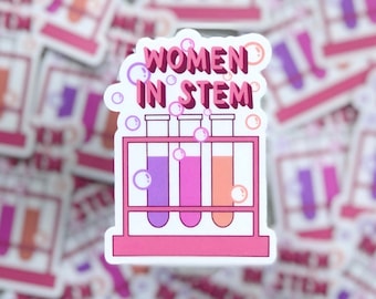 May include: A pink and white sticker with the text "Women in STEM" and a graphic of three test tubes in a rack. The test tubes are filled with purple, pink, and orange liquids.