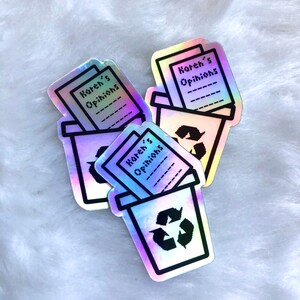 Könnte beinhalten: Drei regenbogenfarbene Aufkleber mit einem schwarzen Umriss eines Mülleimers mit einem Recyclingsymbol und dem Text "Karen's Opinions" auf einem Papierstück im Mülleimer.