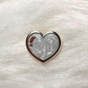 May include: A gold heart-shaped pin with a white enamel fill and a red exclamation point inside.