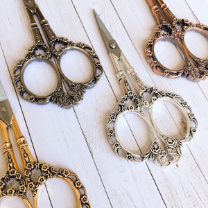 May include: Three pairs of decorative scissors with ornate floral designs. The scissors are silver, gold, and bronze.