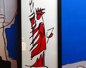 May include: A framed art print featuring a stylized depiction of the Statue of Liberty. The artwork uses bold black outlines and vibrant red and white colors. The print is in a black frame and rests on an orange surface.