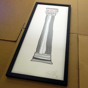 May include: Black framed print of a hand-drawn illustration of a column with a capital. The column is drawn in shades of grey and the capital is red. The print is signed "Jason O" in the bottom right corner.