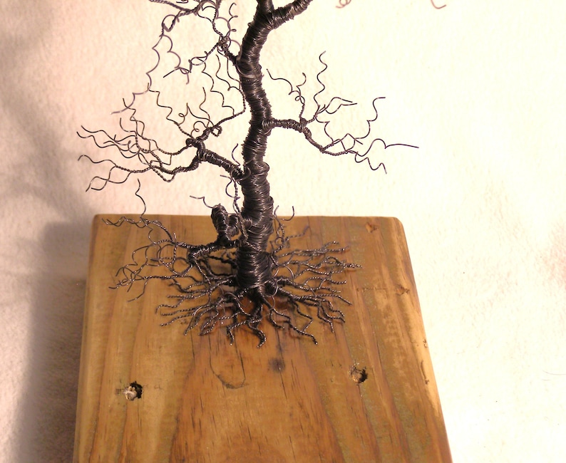 Pode incluir: Uma escultura de arame de uma &aacute;rvore com uma base de madeira marrom. A &aacute;rvore tem um tronco grosso e muitos galhos que s&atilde;o torcidos e encaracolados. As ra&iacute;zes da &aacute;rvore s&atilde;o vis&iacute;veis e se espalham pela base.