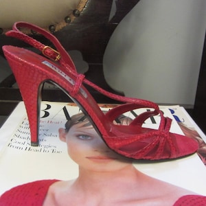 May include: A red high-heeled sandal with a thin strap and a criss-cross design on the front. The sandal is made of a textured material and has a gold buckle on the strap.