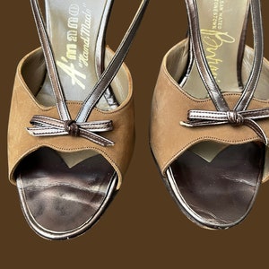 K&ouml;nnte beinhalten: Ein Paar braune Wildledersandalen mit Absatz, einem braunen Lederriemen und einem Schleifendetail. Die Sandalen sind handgefertigt und haben ein goldenes Etikett mit der Aufschrift "Handgefertigt in Italien".