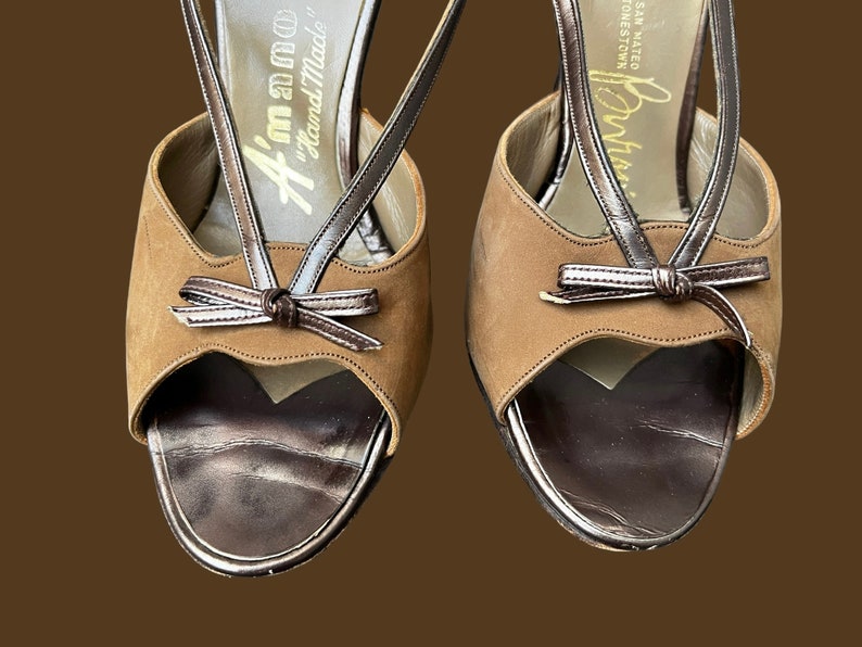 K&ouml;nnte beinhalten: Ein Paar braune Wildledersandalen mit Absatz, einem braunen Lederriemen und einem Schleifendetail. Die Sandalen sind handgefertigt und haben ein goldenes Etikett mit der Aufschrift "Handgefertigt in Italien".