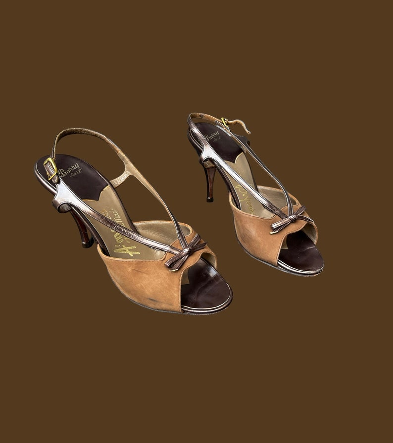 K&ouml;nnte beinhalten: Ein Paar braune und silberne High-Heel-Schuhe mit Peeptoe-Design und Schleifendetail. Die Schuhe sind aus Leder und haben einen Slingback-Riemen.