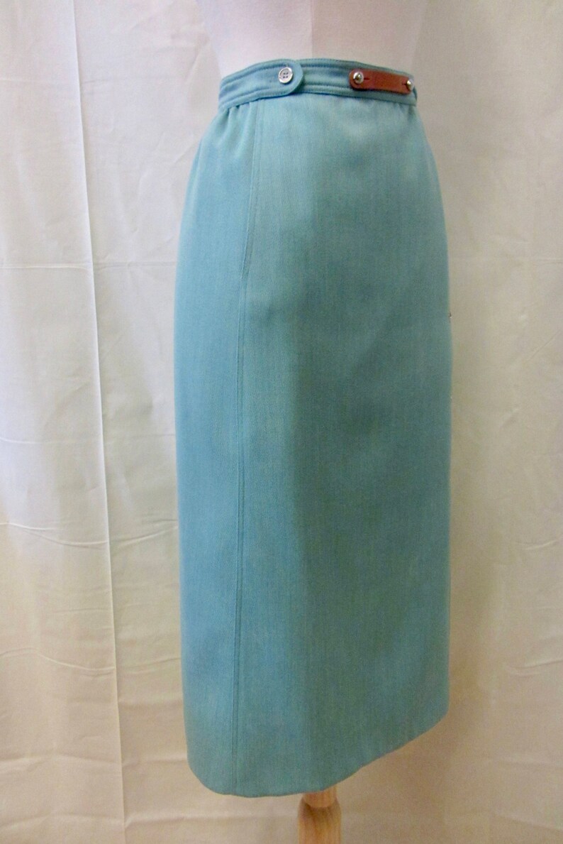 May include: A light blue skirt with a brown leather belt and a silver button. The skirt is knee-length and has a straight silhouette.