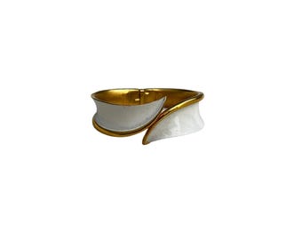 May include: A white and gold bangle bracelet with a curved design. The bracelet is made of metal and has a polished finish.