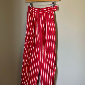 May include: Red and white striped pants with a wide leg and a high waist. The pants have a belt loop and a button closure.