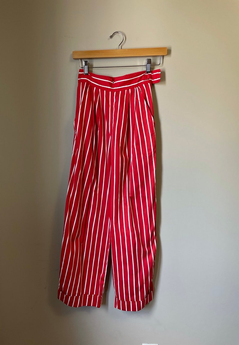 May include: Red and white striped pants with a wide leg and a high waist. The pants have a belt loop and a button closure.