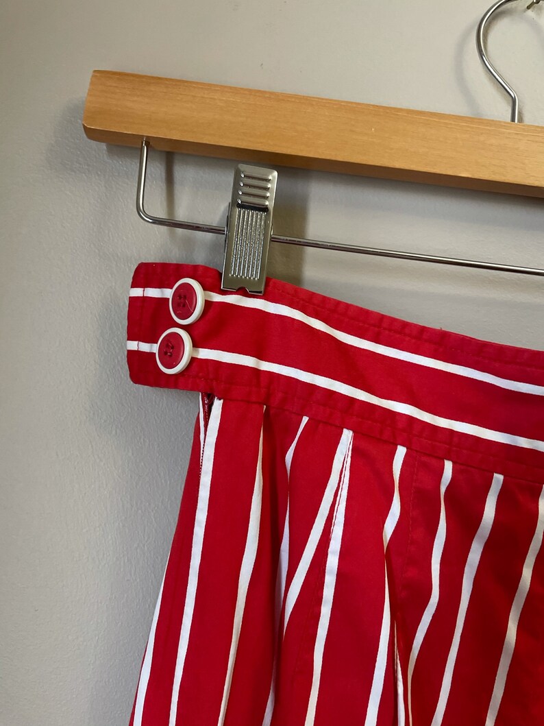May include: Red and white striped skirt with a button closure at the waist. The skirt is pleated and has a wide waistband.