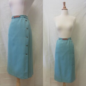 May include: A teal blue wrap skirt with a brown leather belt and button detailing. The skirt is knee-length and has a straight silhouette.
