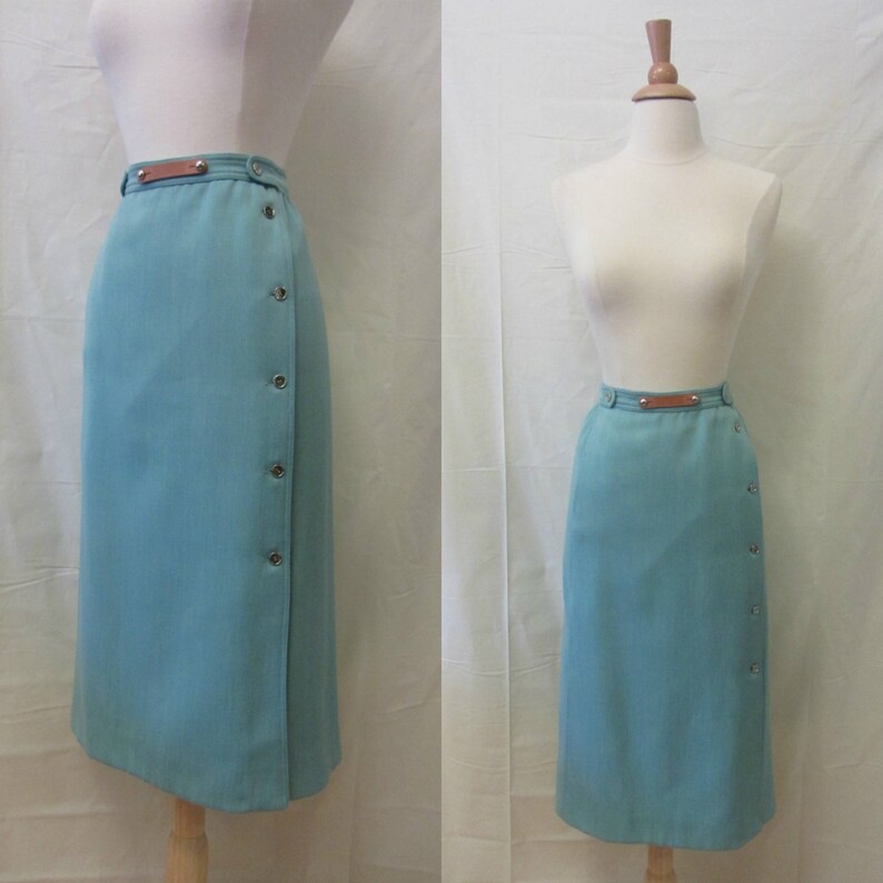 May include: A teal blue wrap skirt with a brown leather belt and button detailing. The skirt is knee-length and has a straight silhouette.