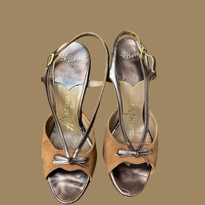 K&ouml;nnte beinhalten: Ein Paar braune Wildledersandalen mit Absatz, goldener Schnalle und Schleifendetail. Die Sandalen sind mit "Barry Last" und "Jeffrey California" gekennzeichnet.