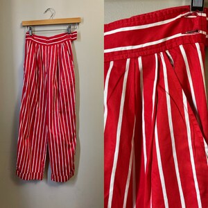 May include: Red and white striped pants with a high waist and pleats. The pants are made of a lightweight fabric and have a relaxed fit.