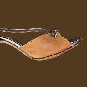 K&ouml;nnte beinhalten: Eine braune Ledersandale mit Absatz, einem Riemen &uuml;ber dem Fu&szlig; und einem Schleifendetail am Kn&ouml;chel.