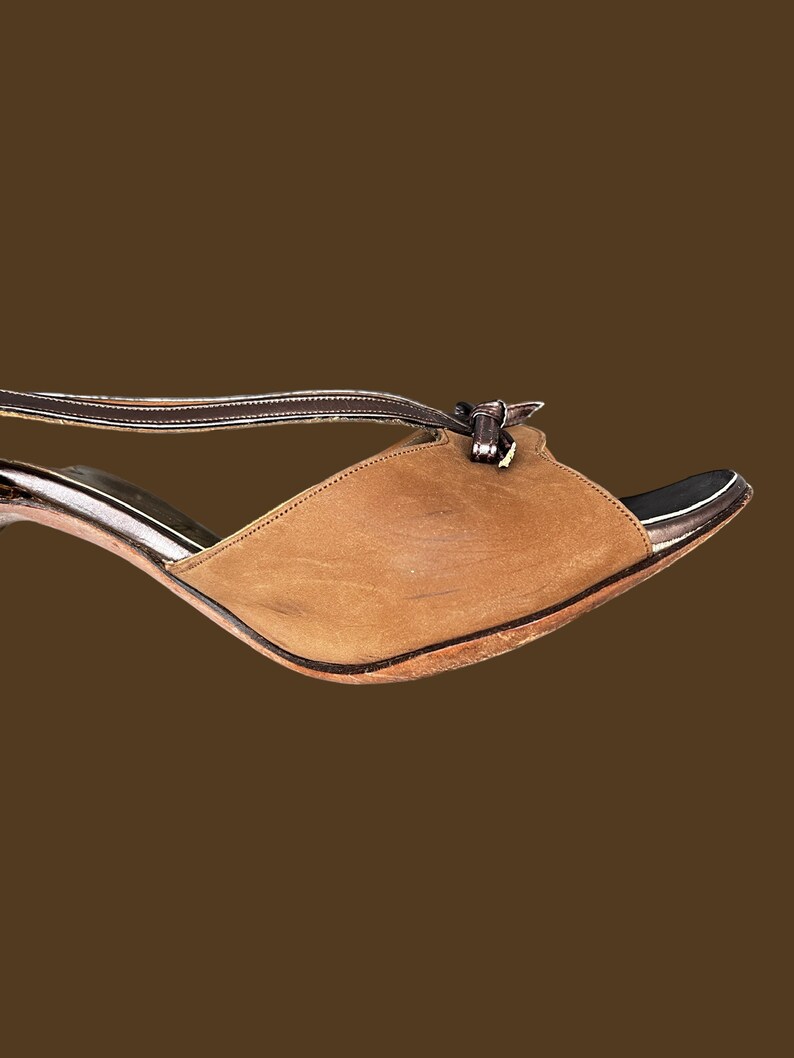 K&ouml;nnte beinhalten: Eine braune Ledersandale mit Absatz, einem Riemen &uuml;ber dem Fu&szlig; und einem Schleifendetail am Kn&ouml;chel.