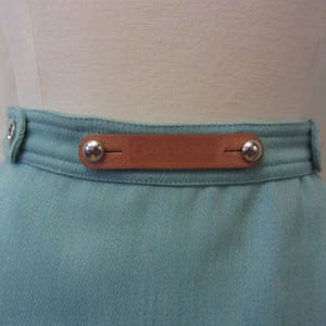 May include: A light blue skirt with a brown leather belt and silver metal buckles. The belt has the word "Couturier" embossed on it.